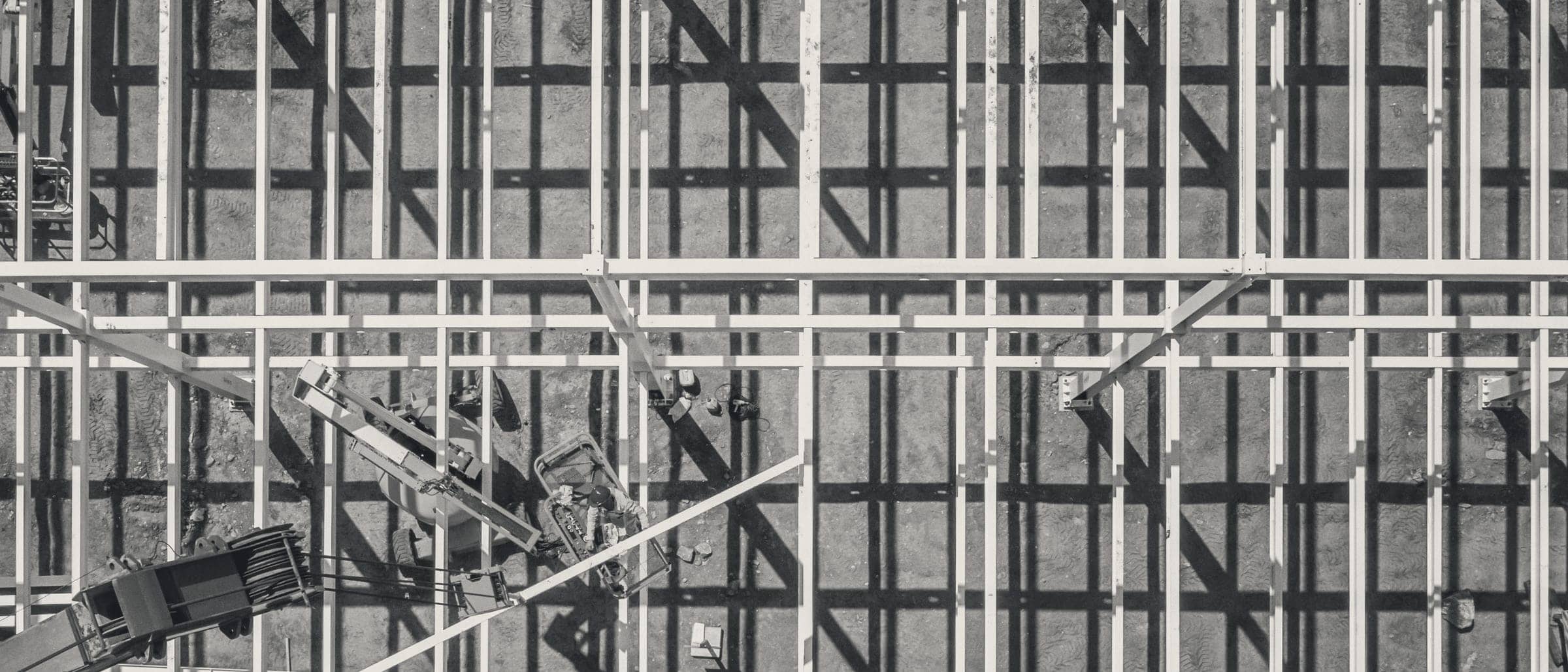Looking straight down on a steel framing grid and its shadows, with one worker in a boom lift.